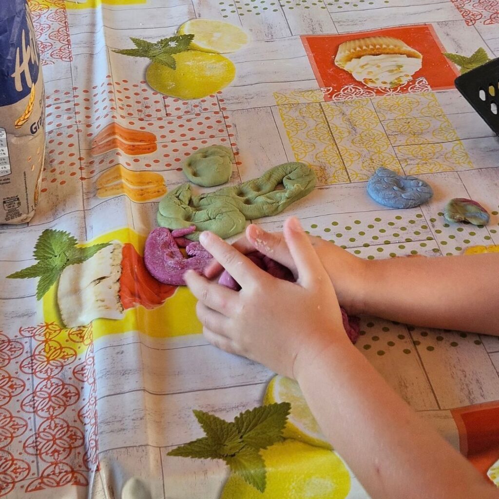 Attività in fattoria per bambini: com'è andata la giornata di Nutriziopoli alla Cascina Teglio? Mani di bambino che impastano farina colorata in un'attività in fattoria per bambini
